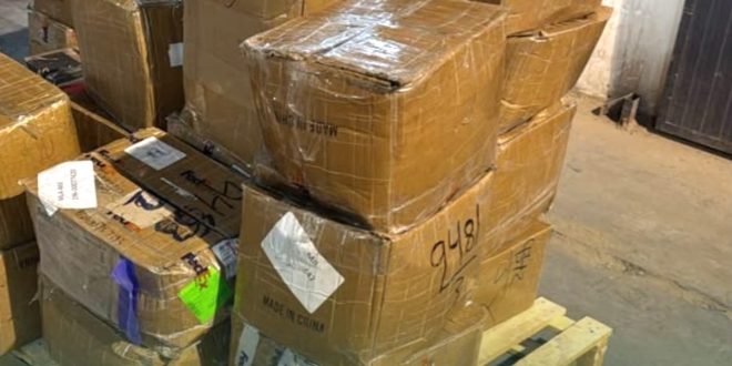 مجموعة من الطرود والكراتين البريدية المغلفة بالبلاستيك والمحملة على منصة خشبية داخل قسم الشحن بمطار معيتيقة الدولي