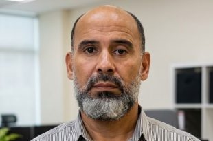 صورة شخصية لـ "علي أبوعزة" رئيس اللجنة العليا للمخابز، يظهر فيها بلحية رمادية وقميص مخطط، ينظر مباشرة إلى الكاميرا داخل مكتب.