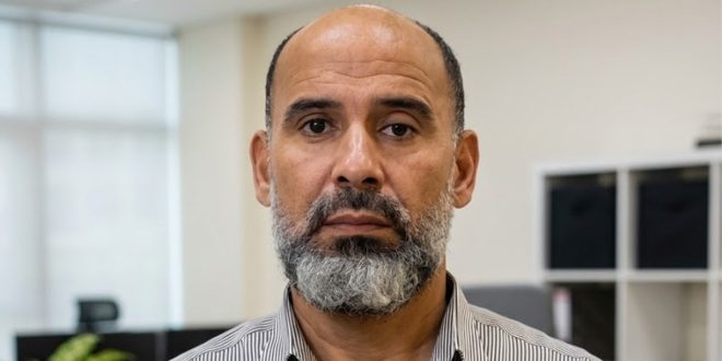صورة شخصية لـ "علي أبوعزة" رئيس اللجنة العليا للمخابز، يظهر فيها بلحية رمادية وقميص مخطط، ينظر مباشرة إلى الكاميرا داخل مكتب.