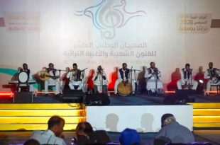 فرقة موسيقية شعبية تؤدي عرضاً حياً على خشبة المسرح خلف شعار المهرجان الوطني العاشر للفنون الشعبية والأغنية التراثية "تراثنا يجمعنا" بمدينة غريان.