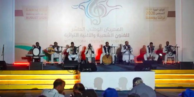فرقة موسيقية شعبية تؤدي عرضاً حياً على خشبة المسرح خلف شعار المهرجان الوطني العاشر للفنون الشعبية والأغنية التراثية "تراثنا يجمعنا" بمدينة غريان.