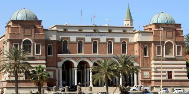المبنى الرئيسي التاريخي لمصرف ليبيا المركزي في طرابلس، بتصميمه المعماري المميز ذي القباب والأقواس والأحجار الطوبية، وأمامه أشجار النخيل وعدد من السيارات المتوقفة