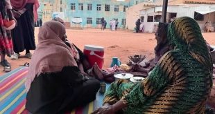 ​"نساء نازحات جالسات على حصير في ساحة عامة بمدينة الأبيض السودانية وسط ظروف إنسانية صعبة وأزمة نزوح متفاقمة."