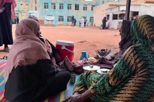 ​"نساء نازحات جالسات على حصير في ساحة عامة بمدينة الأبيض السودانية وسط ظروف إنسانية صعبة وأزمة نزوح متفاقمة."