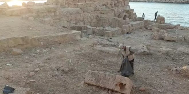 ​شخص يجمع المخلفات في أكياس سوداء بين الآثار الحجرية المطلة على البحر بمدينة سوسة ضمن مشروع تنظيف الآثار.