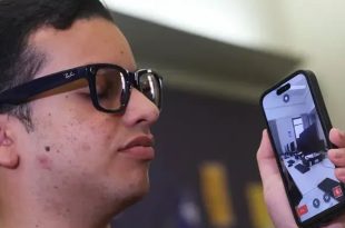 شاب يرتدي نظارة ذكية ويمسك بهاتف ذكي يعرض بثاً مباشراً لكاميرا تظهر الغرفة المحيطة به لاستخدام تطبيق "سكرايب مي