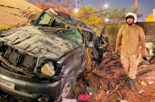 مركبة سوداء تعرضت لأضرار بالغة وتحطم في سقفها وواجهتها جراء حادث سير، وبجوارها رجل أمن يقف بموقع الحادث قرب جسر حي دمشق بطرابلس.