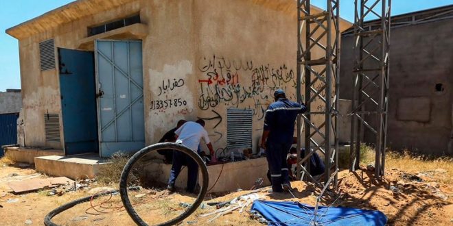 عمال صيانة تابعة للشركة العامة للكهرباء يعملون قرب غرفة محول وأبراج معدنية لإصلاح كوابل متضررة في منطقة أبابوسليم بطرابلس.