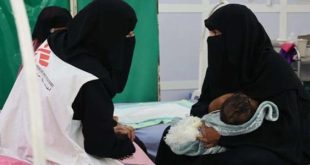 عاملة صحية ترتدي سترة منظمة "أطباء بلا حدود" وتتحدث مع أم يمنية ترتدي النقاب وتحمل طفلها الرضيع داخل مرفق طبي