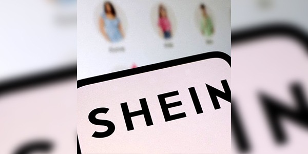 شعار منصة الأزياء السريعة "شي إن" (SHEIN) باللون الأسود على خلفية فاتحة، وتظهر خلفه شاشة تعرض منتجات أزياء