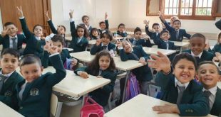 مجموعة من الأطفال والطلاب الليبيين يجلسون داخل الفصل الدراسي مرتديين الزي المهرجاني/المدرسي ويوجهون علامات النصر والترحيب للكاميرا.
