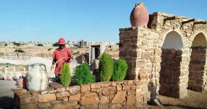 عامل يرتدي قميصاً أحمر وقبعة يقف أثناء أعمال ترميم وتنسيق موقع مسجد أبي نصر التملوشايتي التاريخي في كاباو