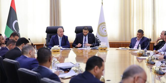 اجتماع حول طاولة مستديرة يضم وزير الدولة لشؤون رئيس الحكومة ووزير الاقتصاد ومسؤولين آخرين بحضور العلم الليبي وشعار الوزارة.