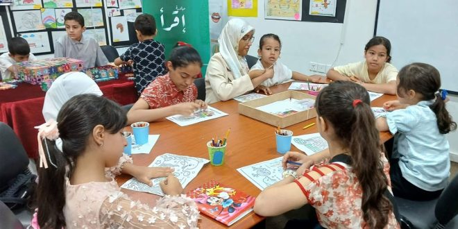 مجموعة من الأطفال واليافعين يجلسون حول طاولة داخل ورشة عمل بالمركز الثقافي إجدابيا يمارسون أنشطة الرسم والتلوين والقراءة بحضور مشرفات.