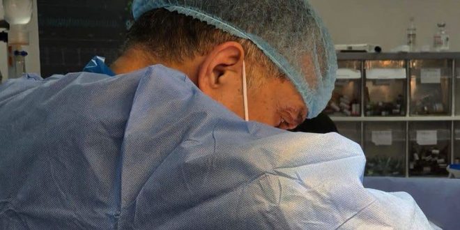 لقطة قريبة لأحد أعضاء الفريق الطبي بمركز بنغازي الطبي يرتدي زي العمليات الأزرق المعقم وغطاء الرأس أثناء التركيز في إجراء عملية جراحية معقدة.