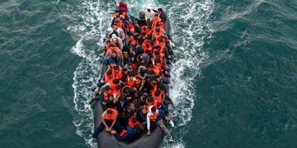 لقطة جوية لقارب مطاطي مكتظ بعشرات المهاجرين الذين يرتدون سترات نجاة برتقالية وسط مياه البحر