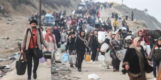حشداً كبيراً من الفلسطينيين يسيرون على طريق مدمر في قطاع غزة، ويحملون ممتلكاتهم الشخصية، في مشهد يعكس النزوح القسري