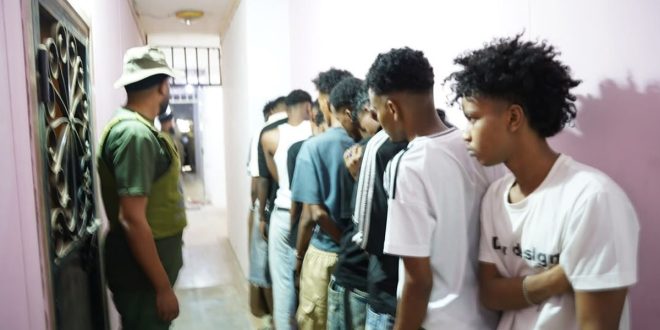 عنصر أمن ليبي يراقب صفاً من العمال الوافدين داخل ممر ضيق خلال حملة تفتيشية لوزارة العمل في طرابلس