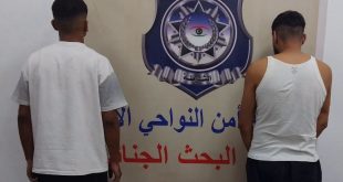 شخصان موقوفان يعطيان ظهرهما للكاميرا يقفان أمام شعار وزارة الداخلية بمديرية أمن النواحي الأربع