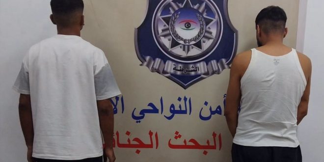 شخصان موقوفان يعطيان ظهرهما للكاميرا يقفان أمام شعار وزارة الداخلية بمديرية أمن النواحي الأربع