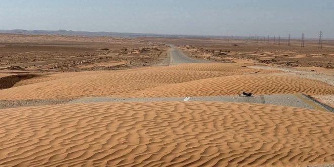 طريق أسفلتي ممتد عبر الصحراء تغطيه كثبان رملية ذهبية تعيق حركة المرور بعد منطقة سيناون