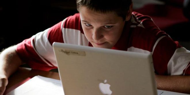صورة طفل يرتدي قميصاً مخططاً بالأحمر والأبيض يجلس أمام حاسوب محمول