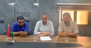 ثلاثة مسؤولين من إدارة مستشفى يفرن يجلسون خلف طاولة اجتماعات خشبية يضعون عليها ورقة بيان رسمي وعلم ليبيا أثناء إلقاء بيان مصور.