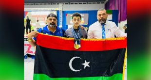 الرباع الليبي عبدالرحيم عزالدين صالح يرتدي الميداليات ويتوسط شخصين يمسكون بالعلم الليبي خلال تتويجه في بطولتي أفريقيا والعرب لرفع الأثقال بمدينة مستغانم الجزائرية