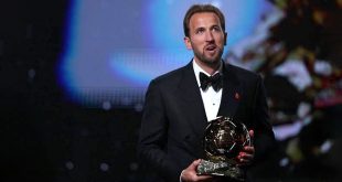 لاعب كرة القدم الإنجليزي هاري كين يرتدي بدلة رسمية أنيقة ويحمل بين يديه جائزة الكرة الذهبية خلال حفل التتويج.