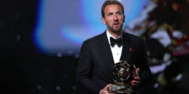 لاعب كرة القدم الإنجليزي هاري كين يرتدي بدلة رسمية أنيقة ويحمل بين يديه جائزة الكرة الذهبية خلال حفل التتويج.