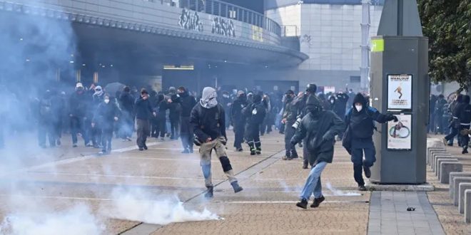 صورة لمجموعة من المتظاهرين والملثمين وسط الشارع مع تصاعد أعمدة الدخان والغاز المسيل للدموع خلال اشتباكات في إحدى المدن الأوروبية