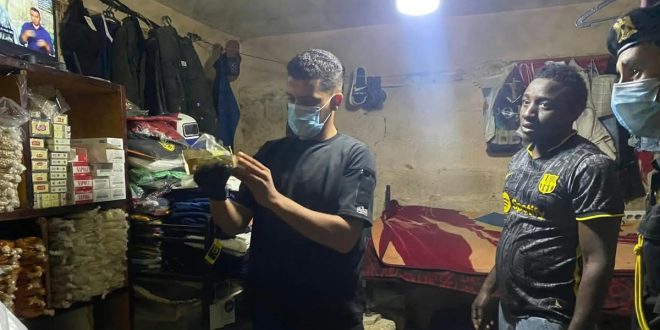 عنصر من دوريات الحرس البلدي يفحص أكياس ومواد في موقع مخالف بحضور أحد العمال المخالفين ورجل أمن