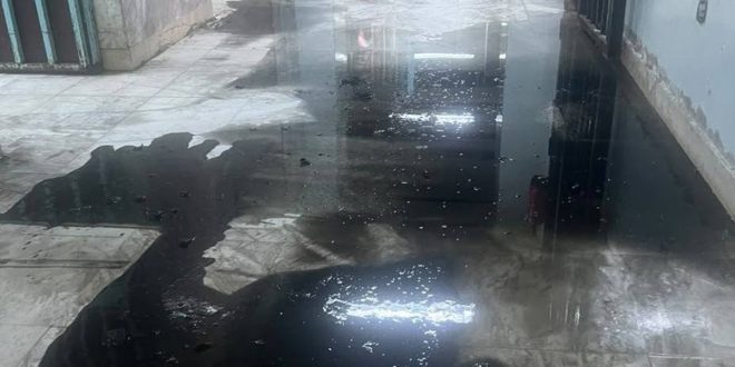 ​صورة لأرضية ممر غارقة بتجمعات المياه مع آثار رطوبة وتآكل في جدران مستشفى طرابلس المركزي.