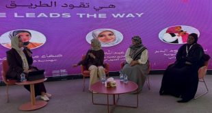 ​لقطة عرضية لمنصة حوارية تجلس عليها أربع سيدات ليبيات محجبات يشاركن في ندوة. خلفهن شاشة عرض أرجوانية كبيرة مضاءة مكتوب عليها باللغتين العربية والإنجليزية: "هي تقود الطريق" و "SHE LEADS THE WAY". تتحدث السيدة التي على اليسار في الميكروفون، بينما تستمع إليها الثلاث الأخريات الجالسات على كراسي وردية مريحة. أمامهن طاولات قهوة صغيرة عليها زجاجات مياه ومحارم. المشهد يمثل إطلاق مبادرة "رايس" للتمكين الرقمي في طرابلس.