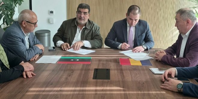 ​يظهر في الصورة اجتماع رسمي يضم مسؤولين من الجانبين الليبي والروماني حول طاولة خشبية مستطيلة، ويتوسط الطاولة علما البلدين (ليبيا ورومانيا) إلى جانب بعض الأوراق والمستندات الخاصة بالاتفاقية. يجلس المشاركون وهم يتابعون أو يوقعون وثائق الاتفاقية المتعلقة بالشهادات الصحية البيطرية وتسهيل توريد اللحوم