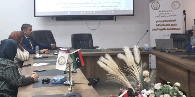 صورة لاجتماع وورشة عمل تربوية تجلس فيها مجموعة من المشاركين حول طاولة اجتماعات خشبية يعلوها العلم الليبي وشعار المصلحة، وتظهر في الخلفية شاشة عرض إلكترونية تعرض شريحة بعنوان "أولاً: الواقع الحالي لنظام الامتحانات والأسئلة"، وبجانبها لافتة تعريفية تابعة لوزارة التربية والتعليم بمصلحة التفتيش والتوجيه التربوي.