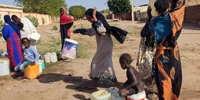 ​"صورة لأطفال ونساء سودانيين في منطقة متأثرة بالصراع، تعبيرًا عن تداعيات هجمات المسيرات والنزوح."